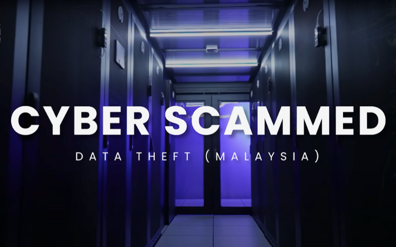 A dimly lit server room with rows of black cabinets illuminated by blue and purple lighting. Large white text overlay reads 'CYBER SCAMMED' with a subtitle below stating 'DATA THEFT (MALAYSIA),' suggesting a focus on cybersecurity threats.